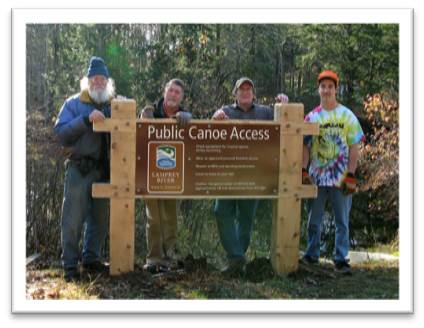 Four men stand behind a newly erected Public Canoe Access sign on the Lamprey River. Pictures courtesy of Jim MacCartney, NPS, Dick Lord and Suzanne Petersen, Lamprey Rivers Advisory Committee Lamprey River, NH.